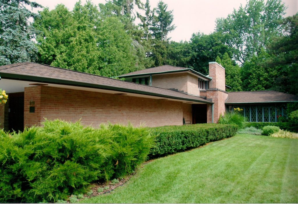 Exterior of a midcentury modern brick home. A walkway leads lined with manicured bushes leads to the front door. 